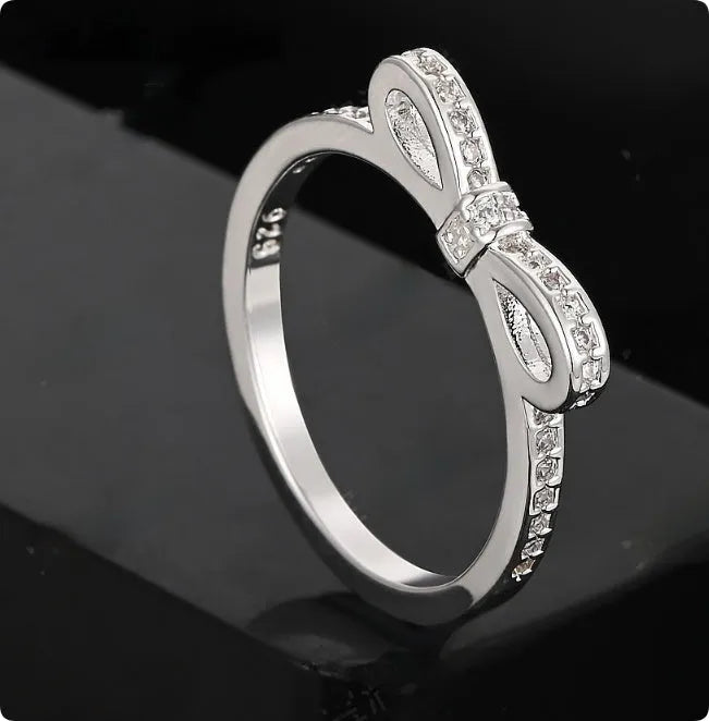 Silver-coloured bow-shaped ring with rhinestone and zircon crystal decoration on a white background.