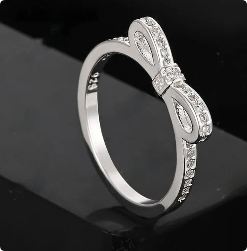 Silver-coloured bow-shaped ring with rhinestone and zircon crystal decoration on a white background.