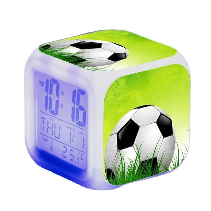 Square football-themed children's alarm clock with mute function on a desk.