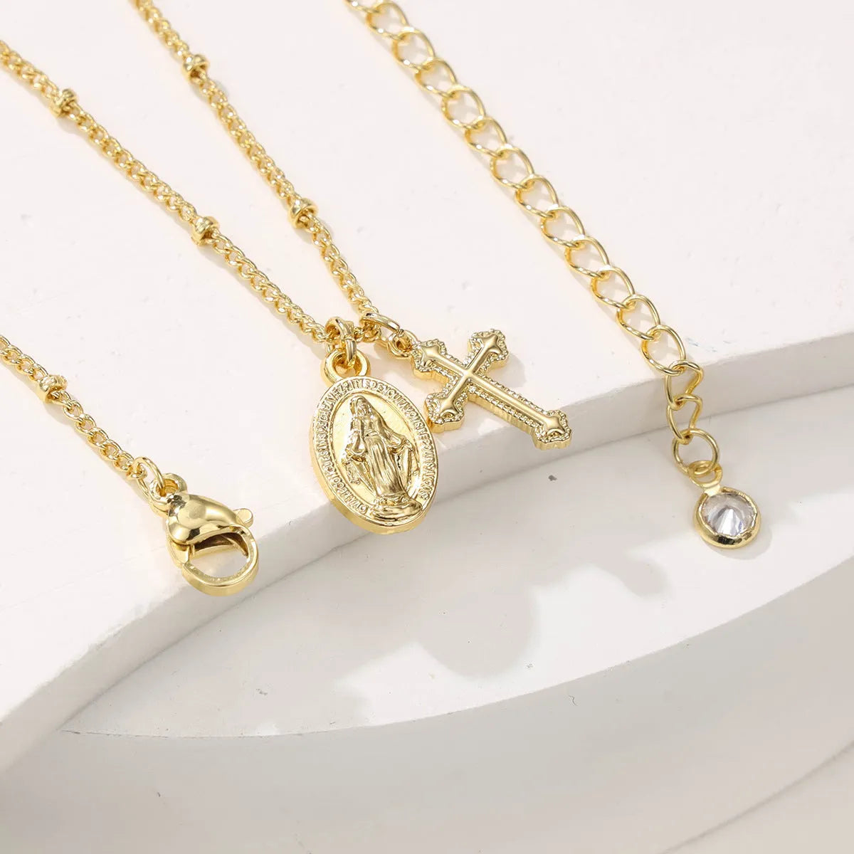 Gold geometric cross and Virgin Mary pendant necklace on display