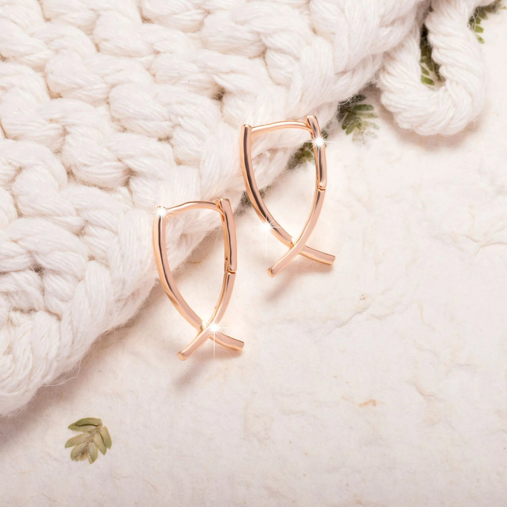 A pair of rose gold coloured cross-shaped earrings on a white background.