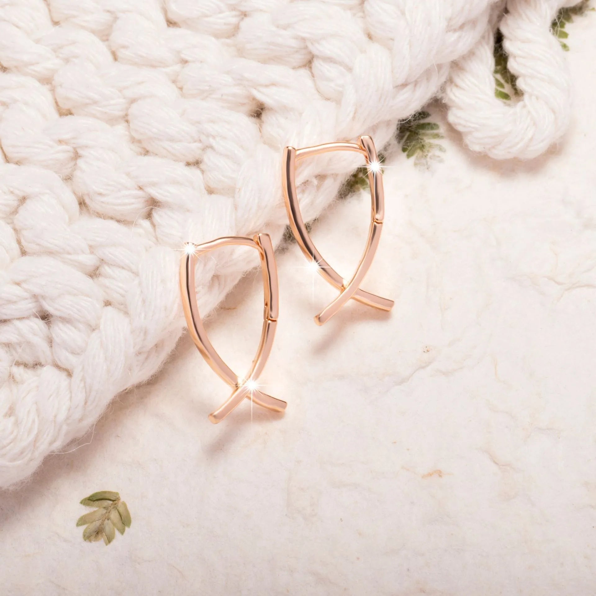A pair of rose gold coloured cross-shaped earrings on a white background.