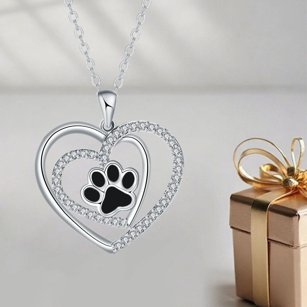 Close-up of a women's heart-shaped copper necklace with a detailed dog paw print pendant on a cross chain.