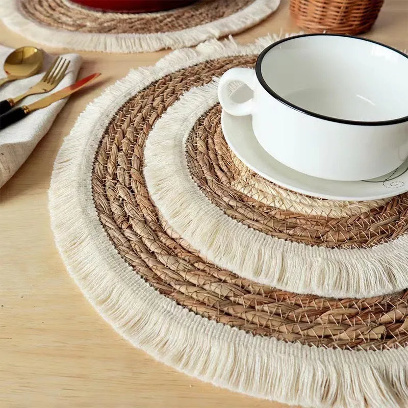 Round natural papyrus placemat with corn rope tassel trim on a wooden table.