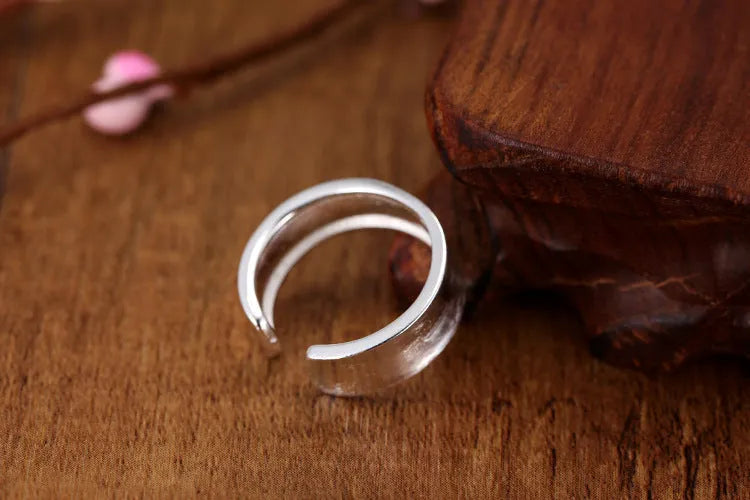Adjustable open ring in frosted sterling silver with a geometric shape on a grey background.