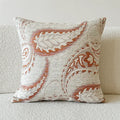 Amber coloured jacquard pillow cover with paisley and floral pattern, shown on a sofa.