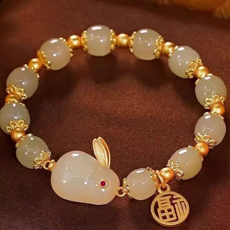 Close-up of a women's black adjustable bracelet with a green jade hare charm, fu character, and lily motif.