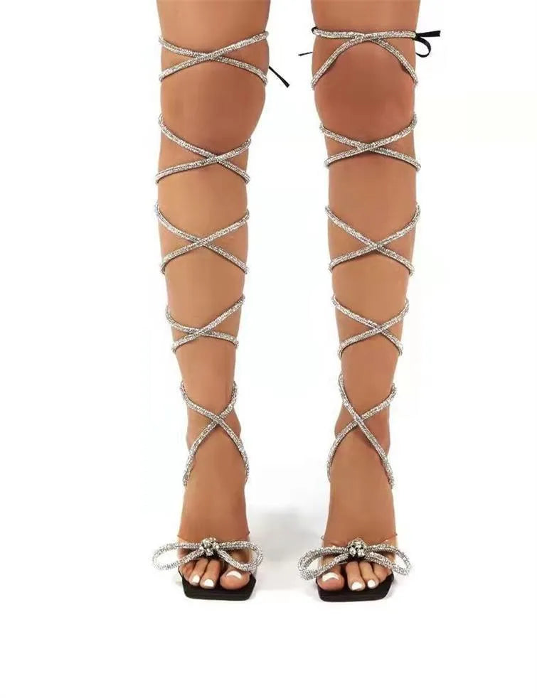 Plus size women's strappy sandal with rhinestone Roman ankle straps and a square toe, shown in black.