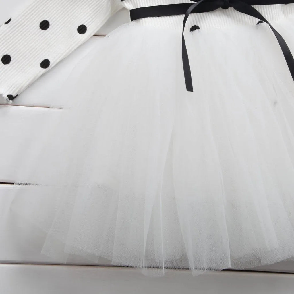 A baby girl wearing a long sleeve black tutu and lace dress for a birthday party.