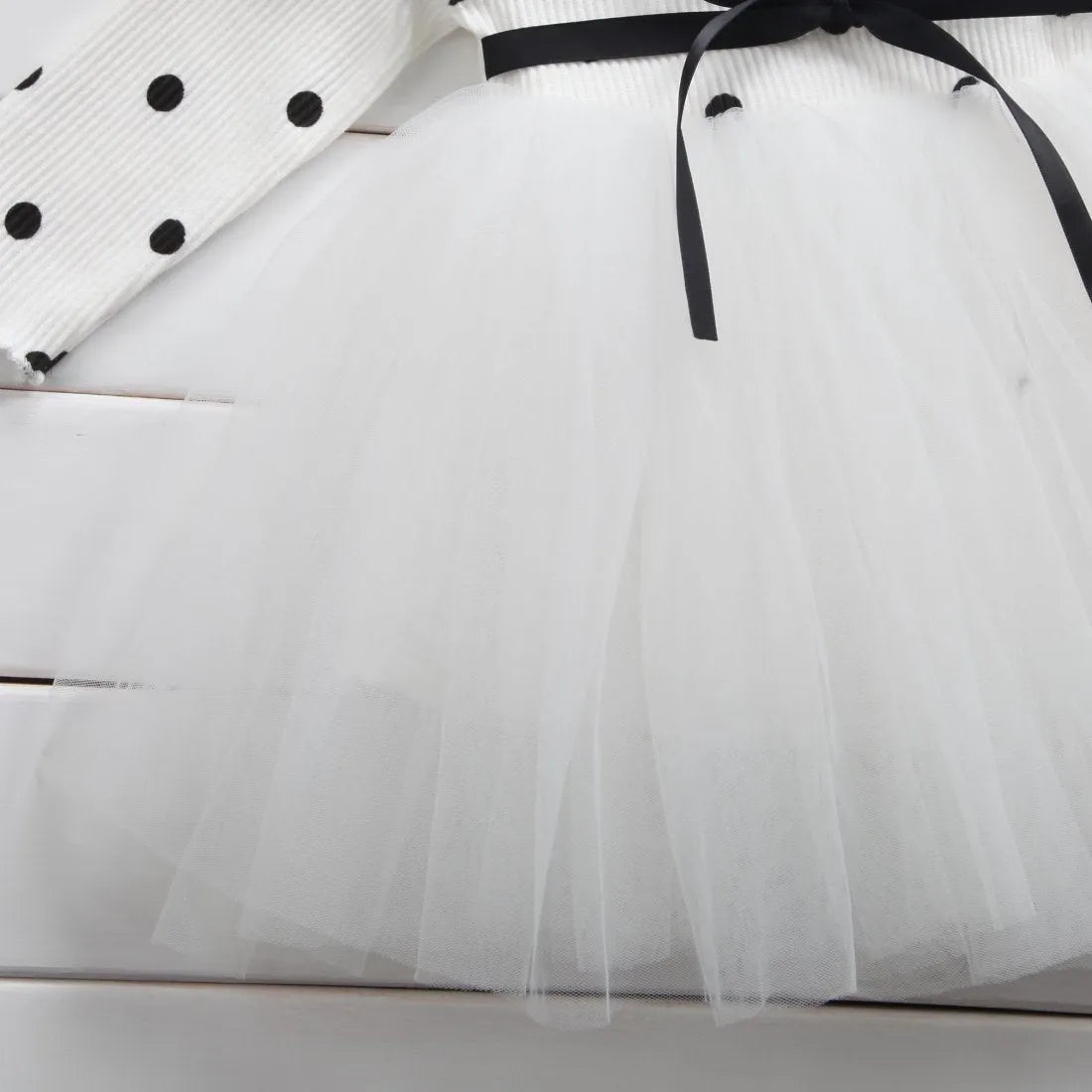 A baby girl wearing a long sleeve black tutu and lace dress for a birthday party.