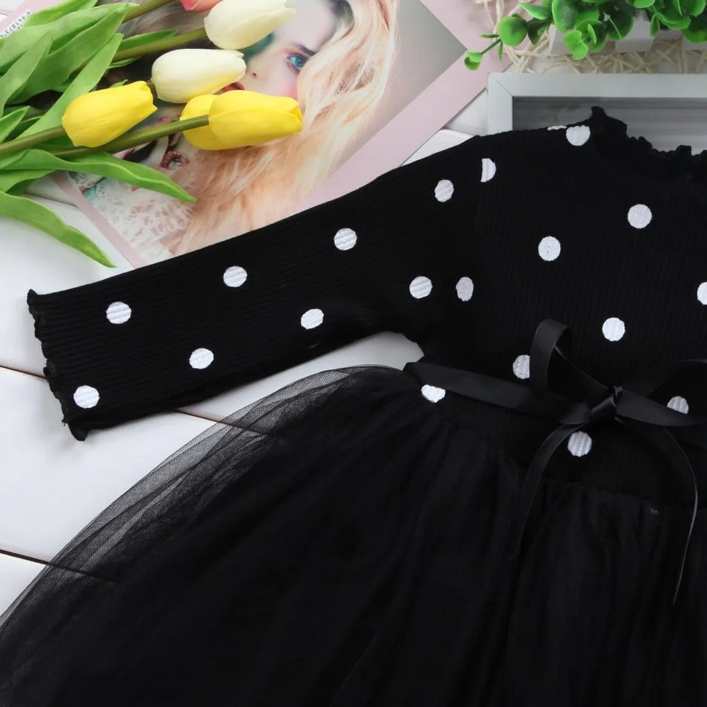 A baby girl wearing a long sleeve black tutu and lace dress for a birthday party.