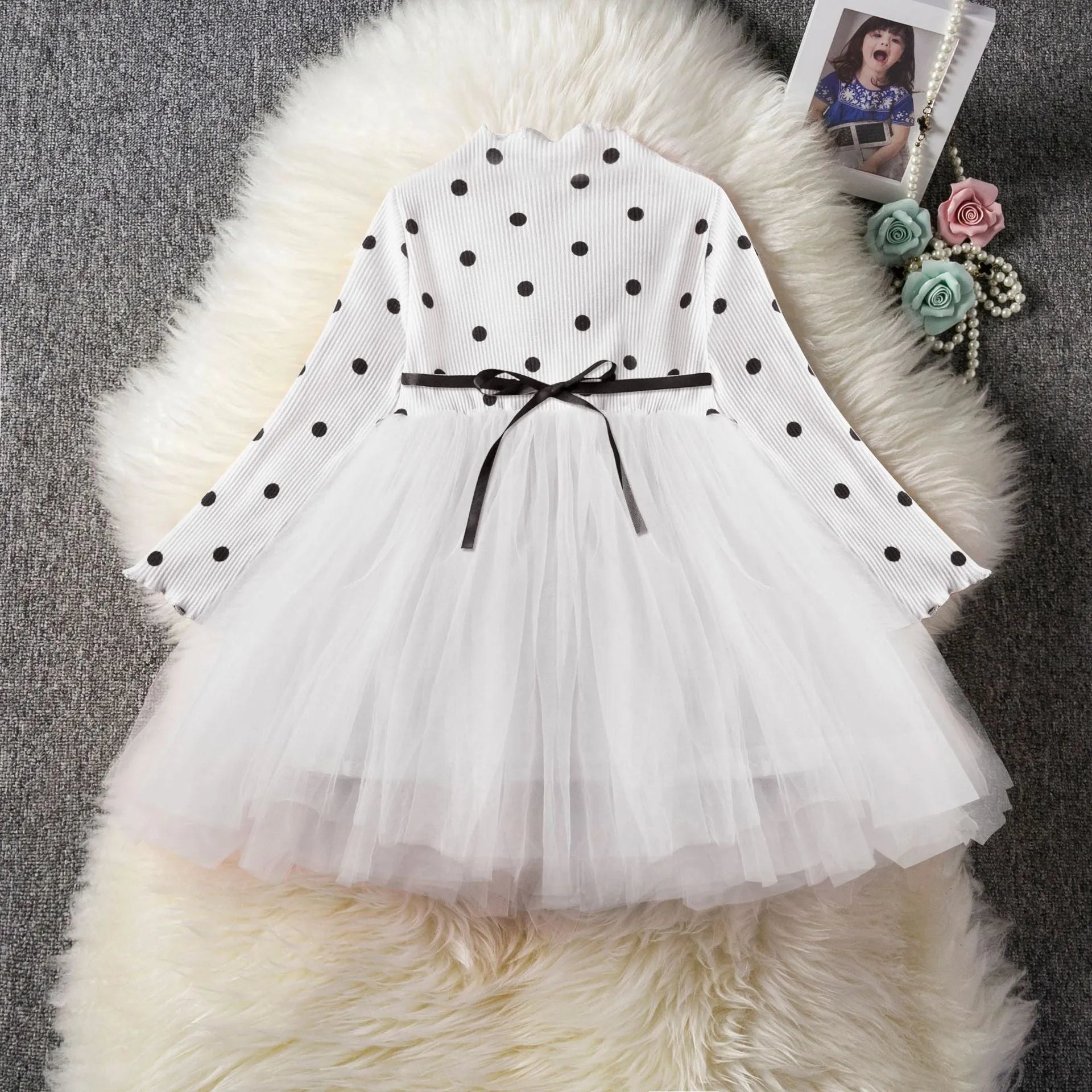 A baby girl wearing a long sleeve black tutu and lace dress for a birthday party.