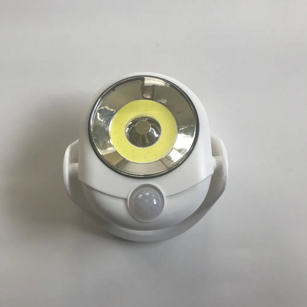 White Atomic Angel induction table lamp with compact ABS plastic body on a table.