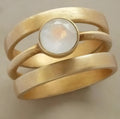 Gold geometric titanium steel ring with micro-inlaid white chalcedony stone on a plain background
