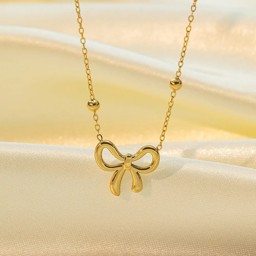 Gold electroplated bow necklace with adjustable chain on white background