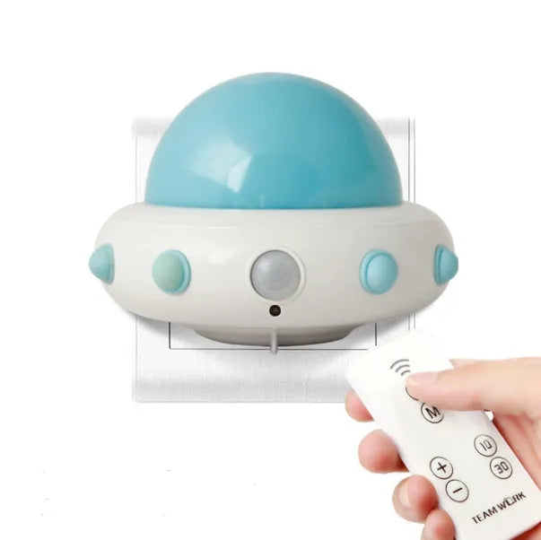 A small blue UFO-shaped bedside night light with a remote control on a wooden table.