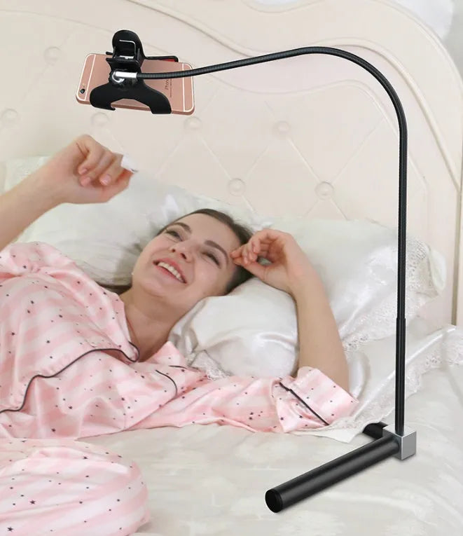 A black mobile phone bed bracket clipped to a bed frame, holding a smartphone in an overhead viewing position.