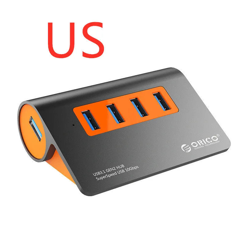 Dark grey aluminium USB hub with four ports, orange accents and detachable cable beside laptop