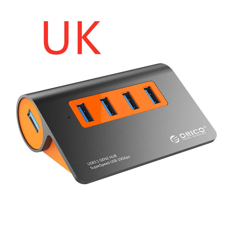 Dark grey aluminium USB hub with four ports, orange accents and detachable cable beside laptop