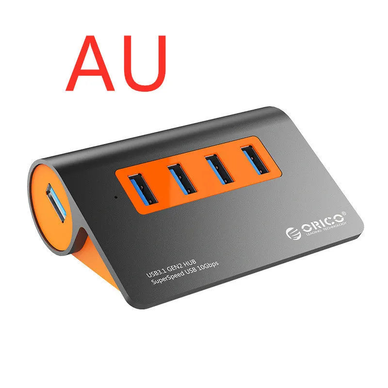 Dark grey aluminium USB hub with four ports, orange accents and detachable cable beside laptop
