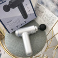 Grey handheld fascia gun muscle massager with USB charging port and adjustable speed controls