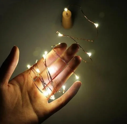 Silver wire LED string lights coiled around wine bottle with illuminated bulbs and bottle stopper fitting