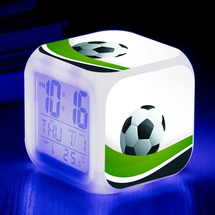 Square football-themed children's alarm clock with mute function on a desk.