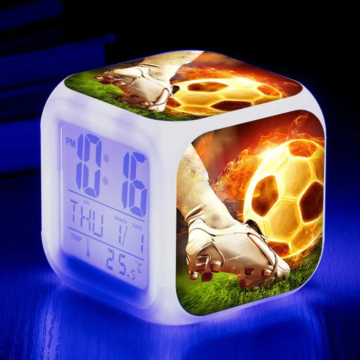 Square football-themed children's alarm clock with mute function on a desk.