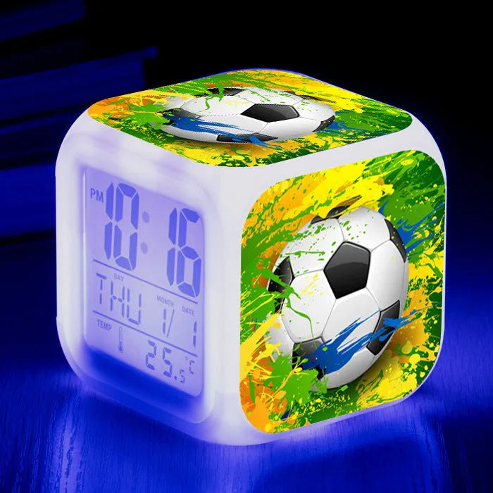 Square football-themed children's alarm clock with mute function on a desk.