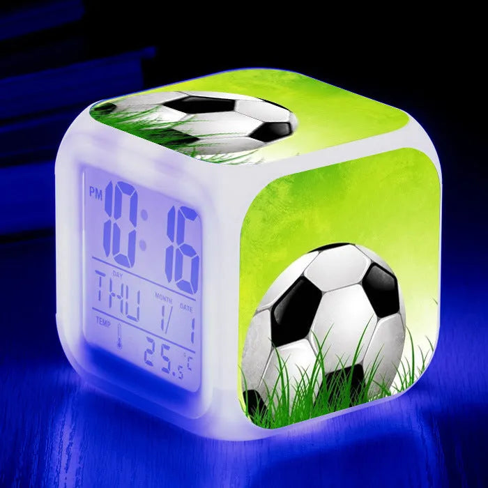 Square football-themed children's alarm clock with mute function on a desk.