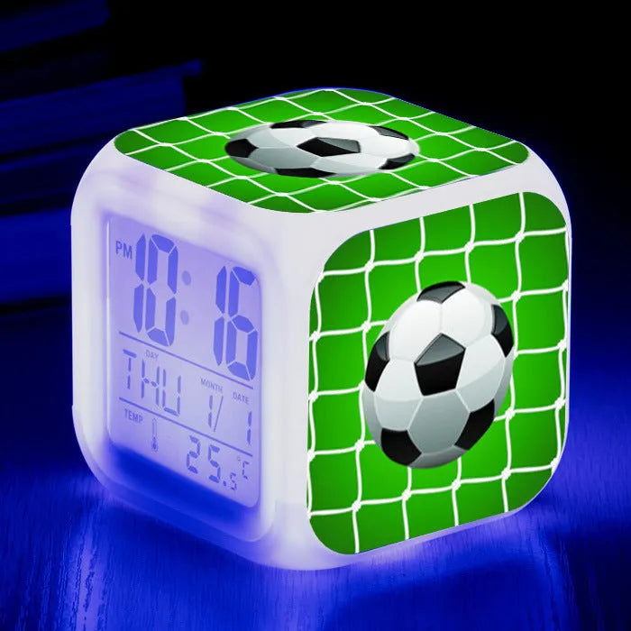 Square football-themed children's alarm clock with mute function on a desk.