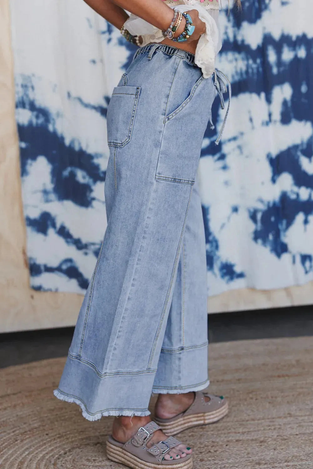 Beau blue wide leg denim trousers with drawstring waist and raw hem on a hanger