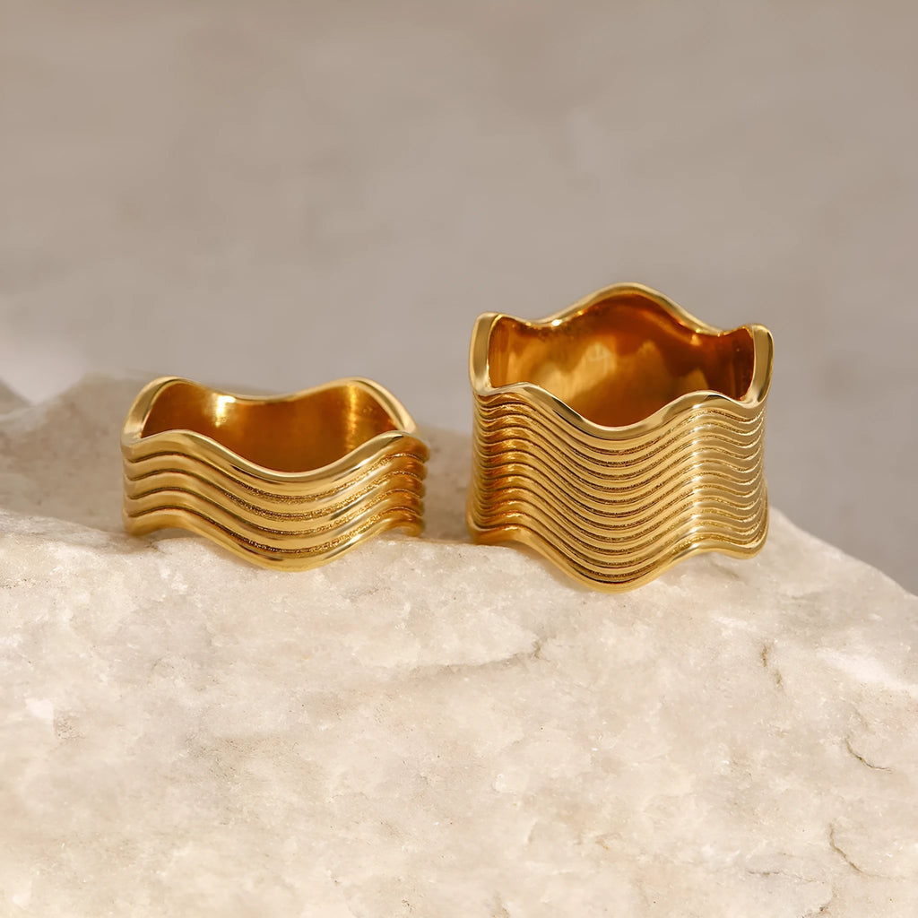 A women's stainless steel ring with a wide, sculptural geometric wave design and an electroplated silver-toned finish.