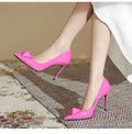 Pink women's pointed toe stiletto high heels with patent leather upper, rivet buckle detail, and a tall thin heel.