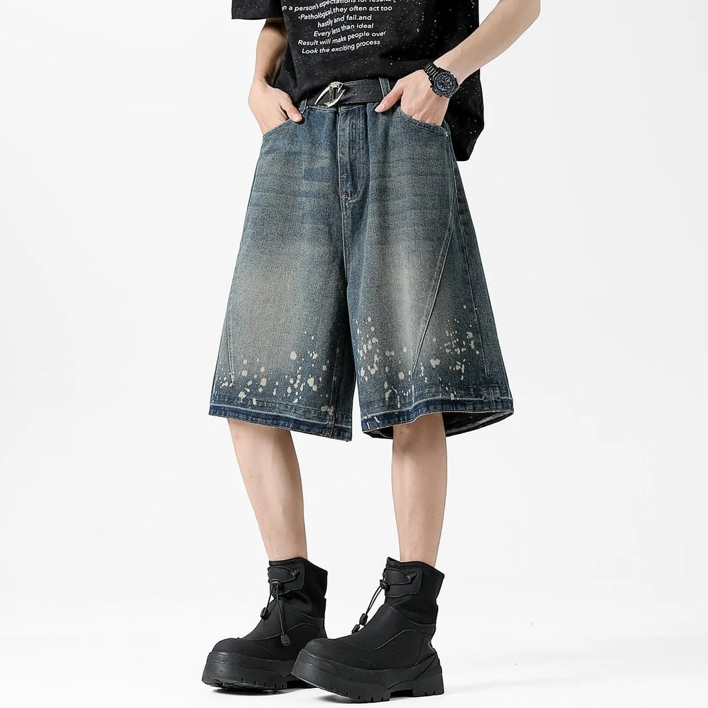 Man wearing retro blue denim shorts with ripped and splash-ink distressing on a straight-leg cut.