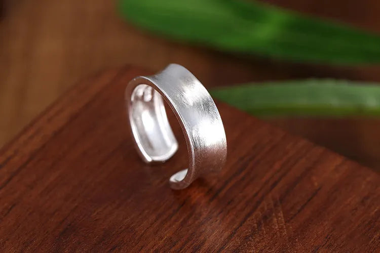 Adjustable open ring in frosted sterling silver with a geometric shape on a grey background.