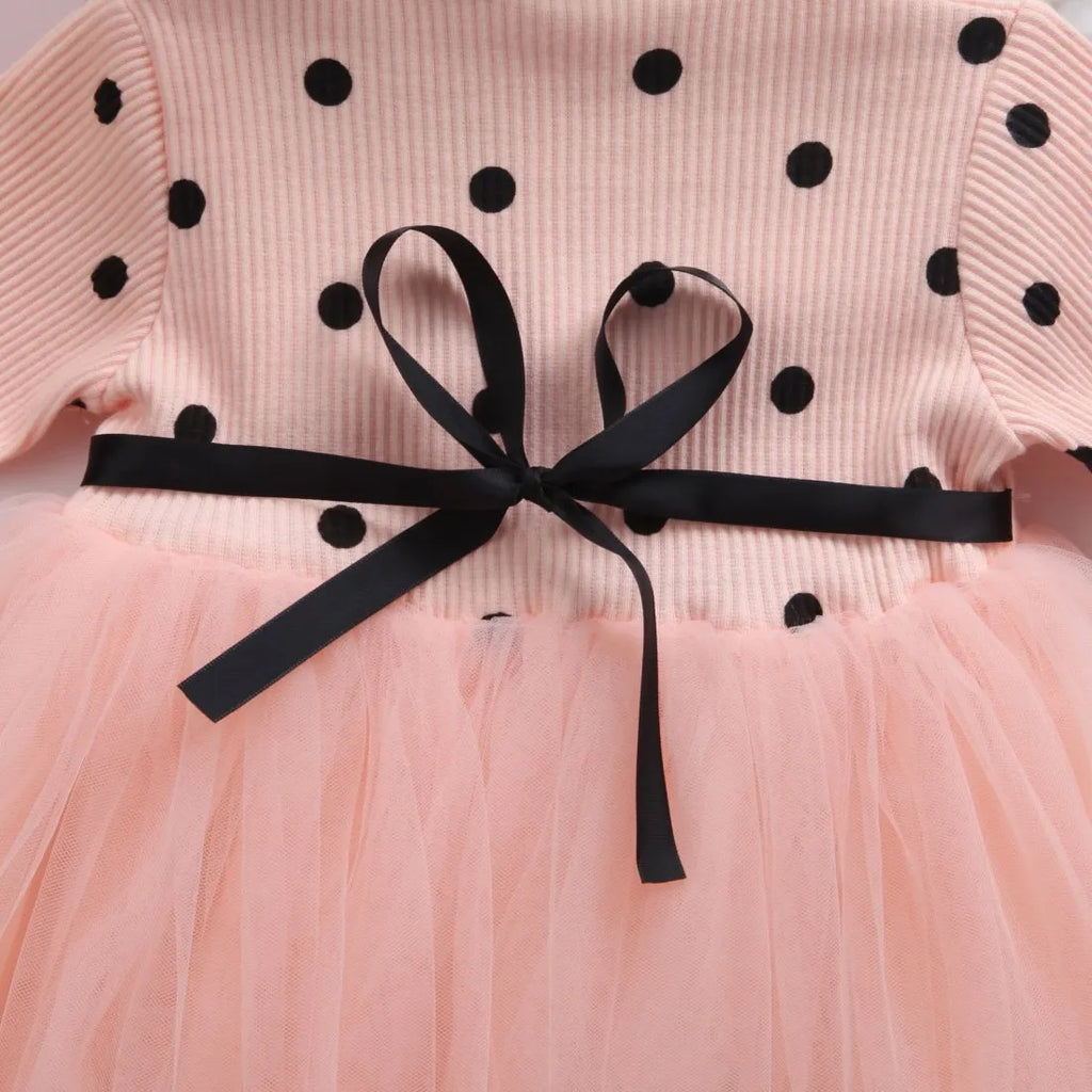 A baby girl wearing a long sleeve black tutu and lace dress for a birthday party.