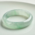 Light green polished jade bracelet in a natural style on a wrist.