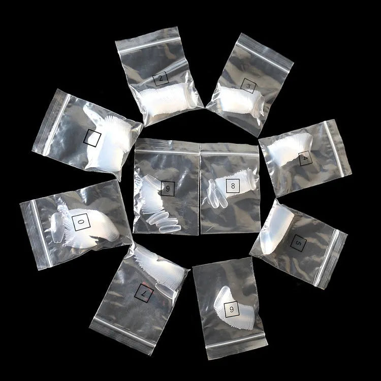 500 clear acrylic false nails in assorted sizes arranged next to application brush and bottle.