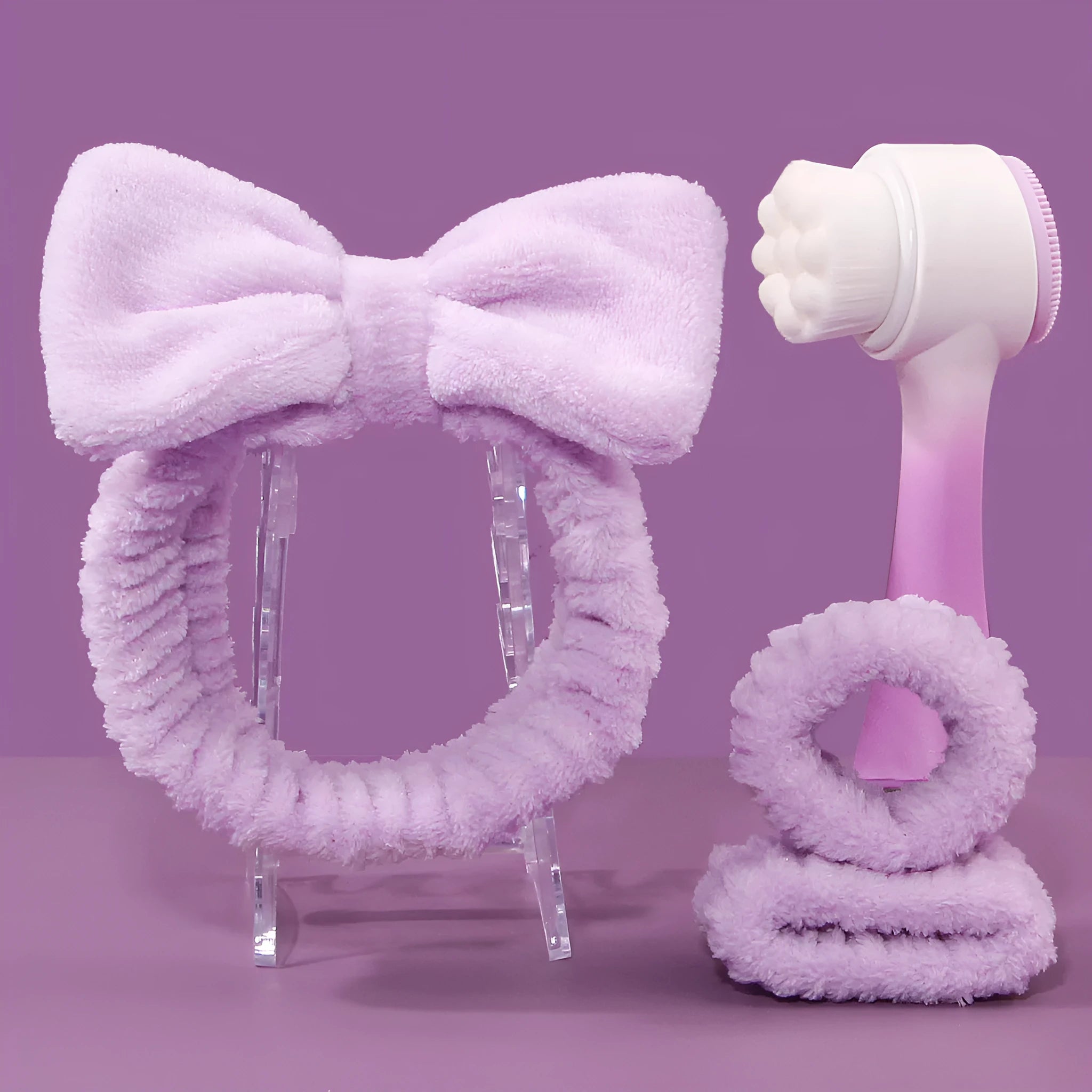 Keep dry facial brush set with plastic handle, coral fleece hair band, and stack of purple and pink face wash sponge suits.