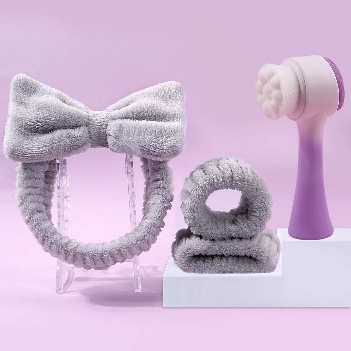 Keep dry facial brush set with plastic handle, coral fleece hair band, and stack of purple and pink face wash sponge suits.