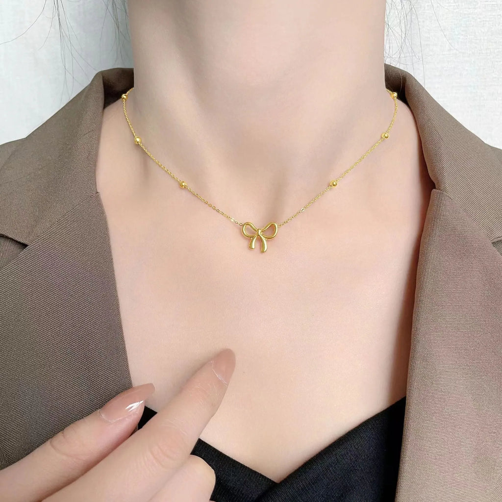 Gold electroplated bow necklace with adjustable chain on white background