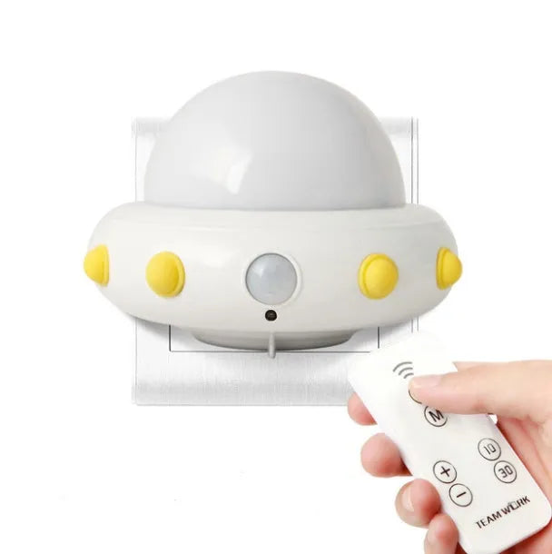 A small blue UFO-shaped bedside night light with a remote control on a wooden table.