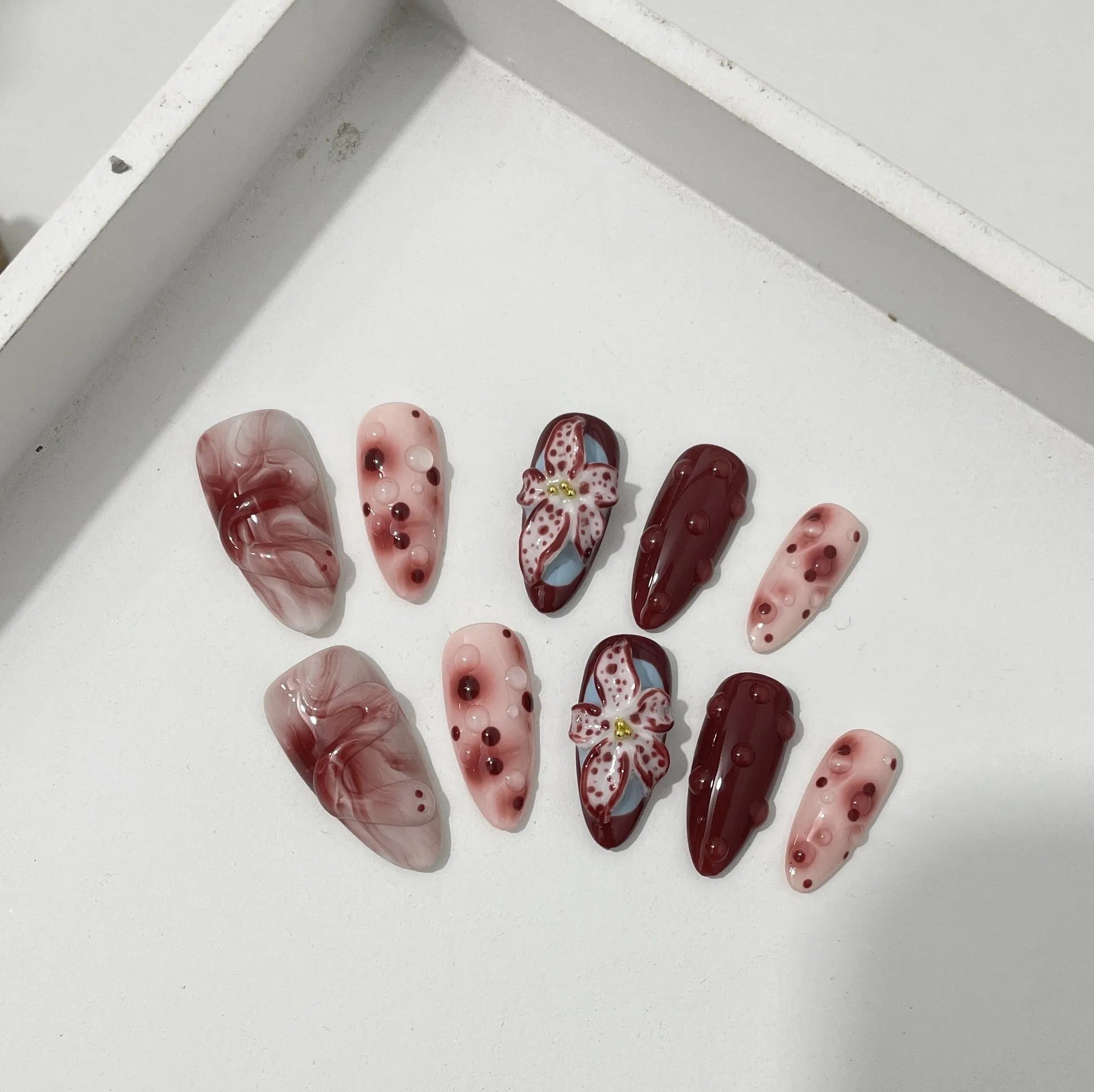 Almond-coloured false nails with hand-painted 3D carved rose designs, shown in medium length.
