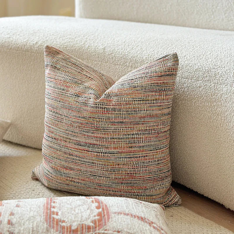 Amber coloured jacquard pillow cover with paisley and floral pattern, shown on a sofa.