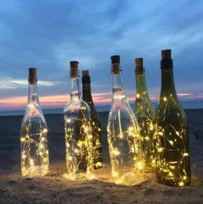 Silver wire LED string lights coiled around wine bottle with illuminated bulbs and bottle stopper fitting