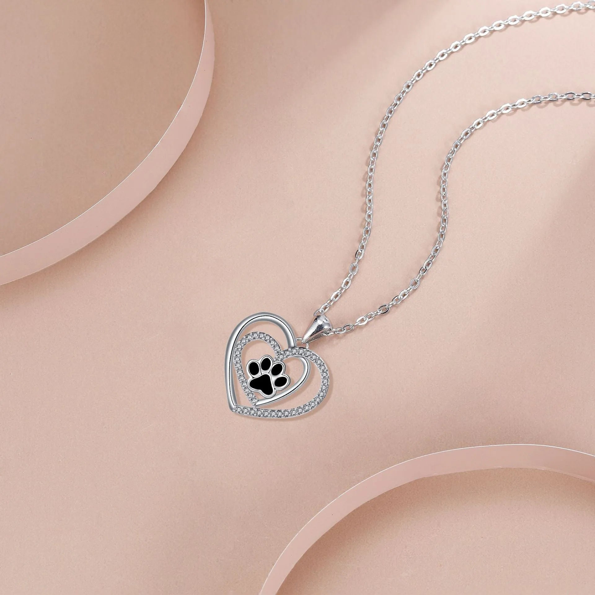 Close-up of a women's heart-shaped copper necklace with a detailed dog paw print pendant on a cross chain.