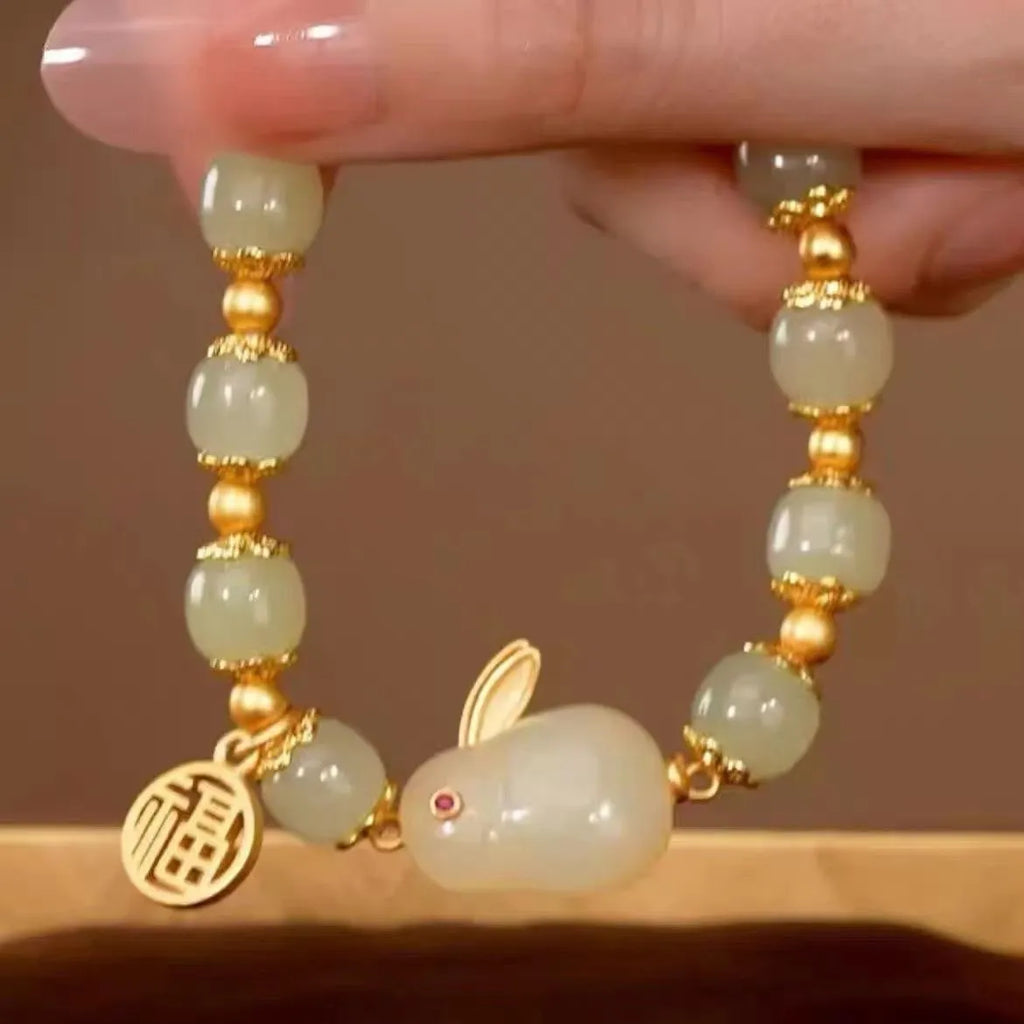Close-up of a women's black adjustable bracelet with a green jade hare charm, fu character, and lily motif.