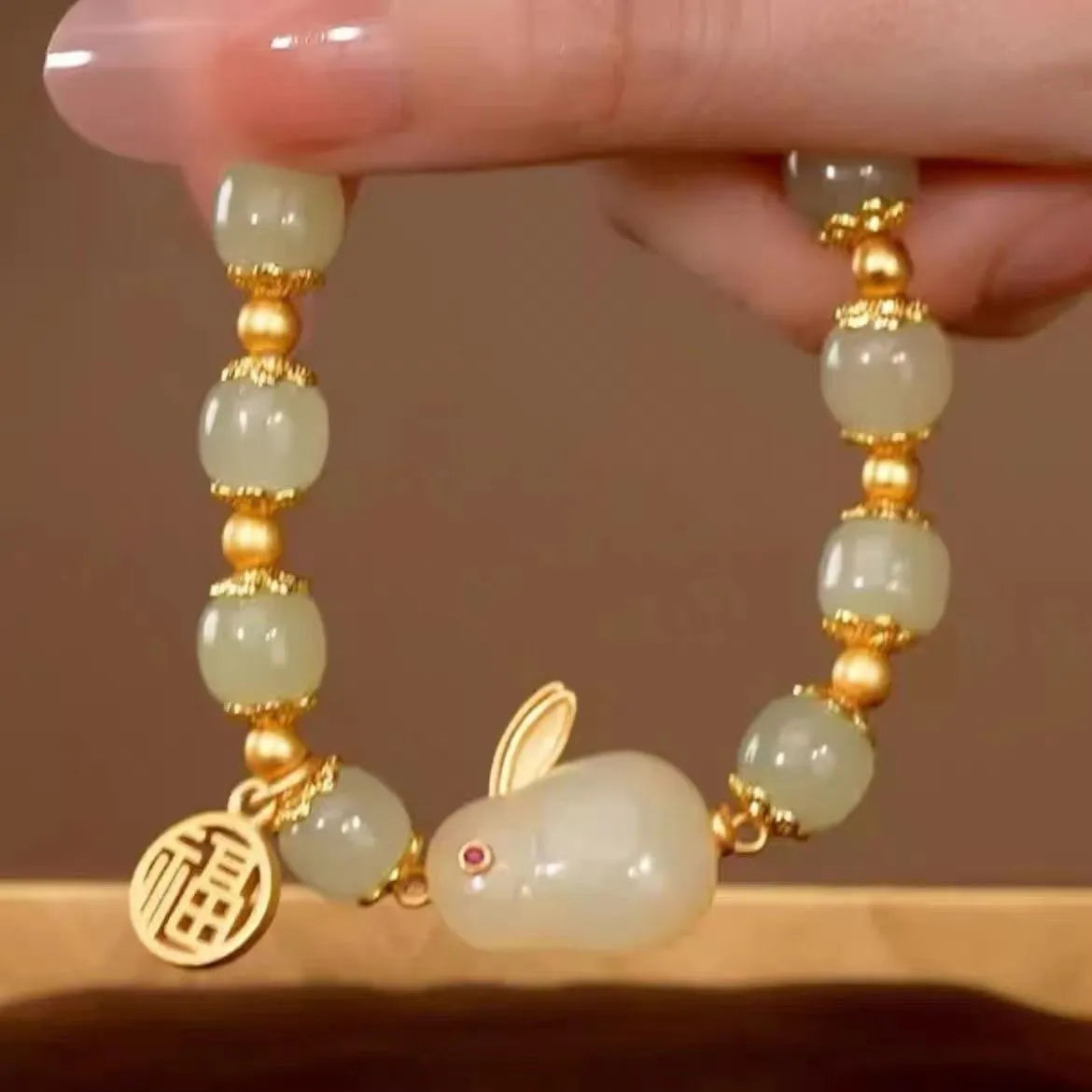 Close-up of a women's black adjustable bracelet with a green jade hare charm, fu character, and lily motif.