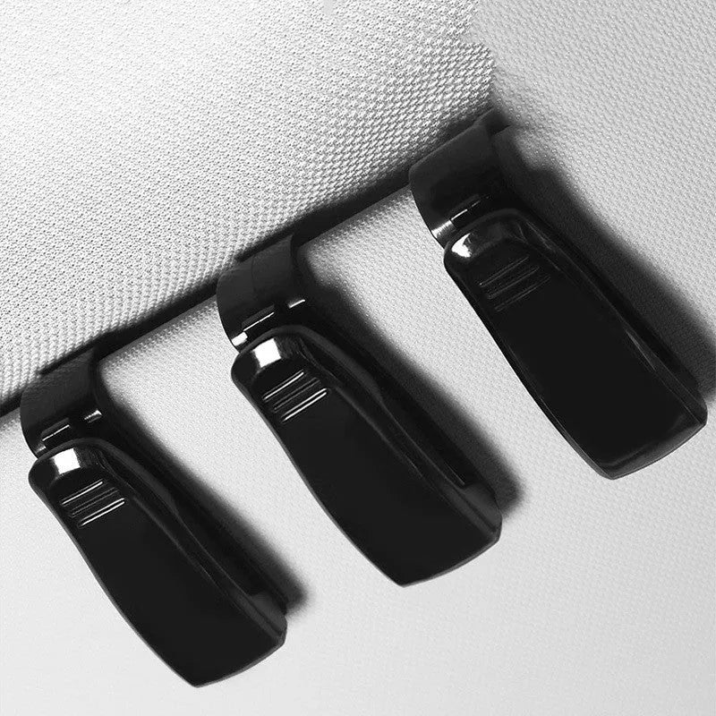 Black plastic clip for car sun visor holding a pair of glasses and a ticket.
